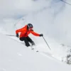 Woman smiles as she makes her way down the mountain on skis, with snow spraying around her.