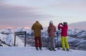 Three skiers pause to take pictures of the sunrise on the slopes.